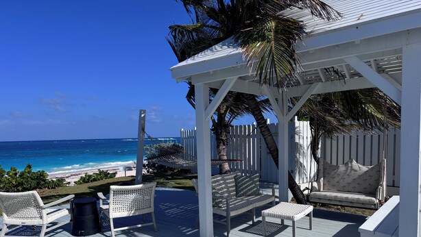 A wooden deck with white wicker furniture, a white gazebo, and a view of the ocean. - Spinney Dune-Beachfront Cottage in the Heart of Hope Town With Harbour Views (Hope Town)