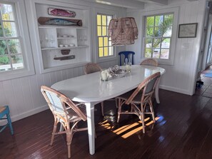 Uma sala de jantar com uma mesa branca, cadeiras de vime e um lustre.
