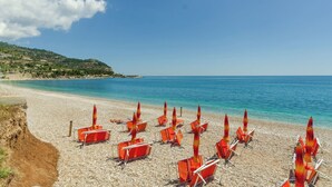 A beach with rows of orange beach chairs and umbrellas, a clear blue sky, and a calm sea.