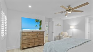 Een slaapkamer met een bed, een dressoir, een plafondventilator, een televisie en uitzicht op het strand.