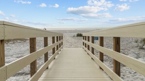 Ein Holzsteg führt zu einem Strand unter blauem Himmel.