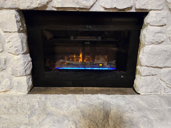 Una chimenea de piedra con frente de vidrio, mostrando un fuego ardiendo en su interior.