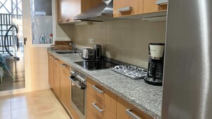 A modern kitchen with wooden cabinets, a stainless steel range hood, a built-in oven, a coffee maker, and a patterned cutting board.