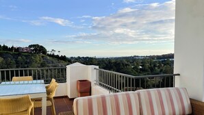 A balcony with wicker furniture, a striped sofa, and a view of a hilly landscape.