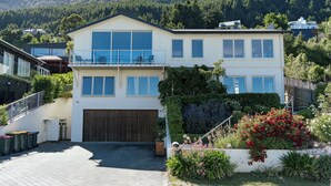 A two-story house with a balcony, a garage, and a garden with various plants and flowers.