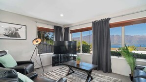 A modern living room with a flat-screen TV, leather sofas, a coffee table, and a large window offering a mountain view.