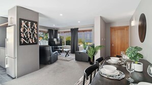 A modern living room with a sofa, TV, and dining area with a table set for two.