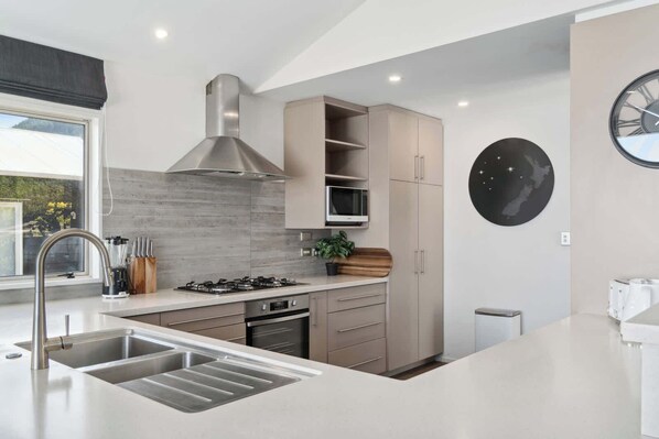 Una cocina moderna con un lavamanos de acero inoxidable, una estufa a gas y un horno empotrado. Se aprecia una ventana con vista a zonas verdes.