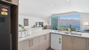 A modern kitchen with a dishwasher, a refrigerator, and a window overlooking a scenic view.