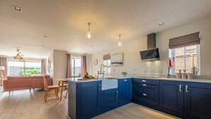 Une cuisine moderne avec des meubles bleus, une table à manger en bois et une vue sur l’extérieur.