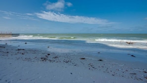 Ein Strand mit Wellen, blauem Himmel und einem Steg im Hintergrund.