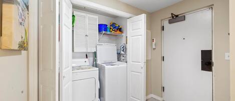 A laundry room with a washing machine, dryer, and shelves with cleaning supplies.