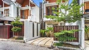 Un edificio residencial moderno con varios balcones, un camino pavimentado y un pequeño jardín.
