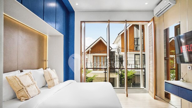 Un dormitorio moderno con una cama grande, un televisor y vistas a casas vecinas a través de un ventanal.