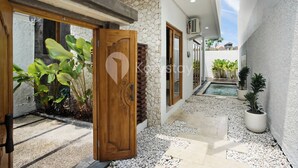 Una casa moderna con un muro de piedra, una puerta de madera y un pequeño jardín con plantas en macetas.