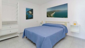 A bedroom with a bed, a white dresser, a shelf with a lamp, and two framed pictures on the wall. - Villa Lucia - Bilo 4 Mandarin - ground floor (Puglia)