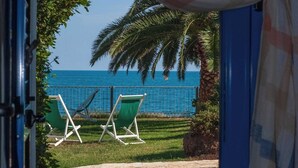 A view through a doorway to a pool area with two lounge chairs facing the ocean, palm trees, and a clear blue sky. - Villa Lucia - Bilo 4 Mandarin - ground floor (Puglia)