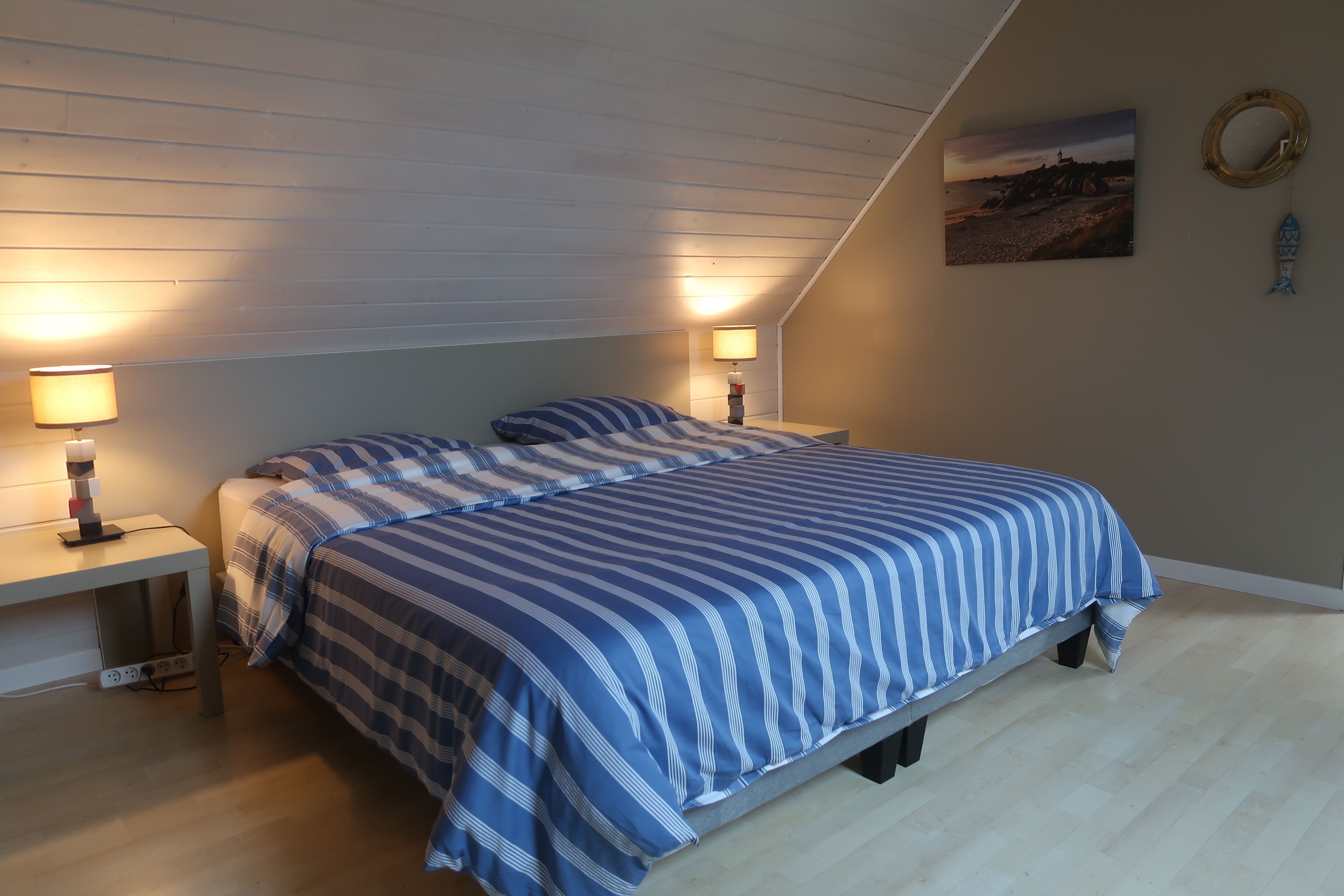 Un dormitorio con una cama, dos mesitas de noche, una lámpara, un cuadro y un adorno con forma de pez.
