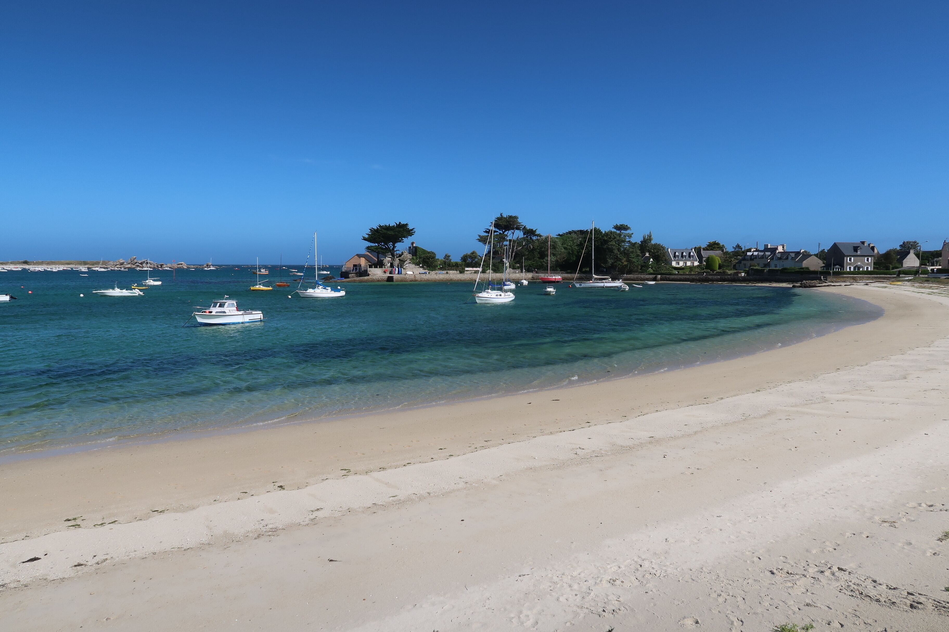 A beach with clear turquoise water, boats, and houses along the shore.