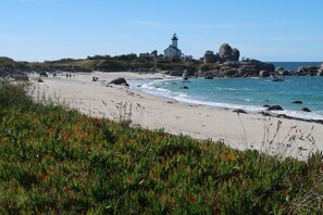 Escena costera con un faro, costa rocosa y playa.