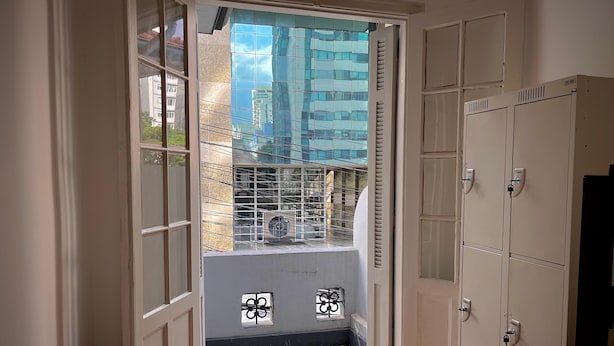 Un pasillo estrecho con una puerta de cristal que da a un balcón con piso estampado y barandilla de metal.