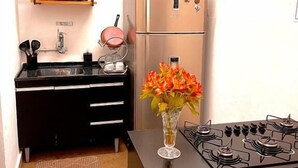 Una cocina compacta con encimera negra, estufa a gas, refrigerador, microondas y cafetera en un estante.