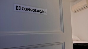 Una habitación con un cartel que dice "CONSOLAÇÃO" en la pared, un equipo de aire acondicionado y una cama individual.