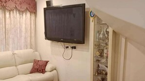 Een woonkamer met een bank, een salontafel, een flatscreen televisie aan de muur en een decoratieve plank met diverse objecten.