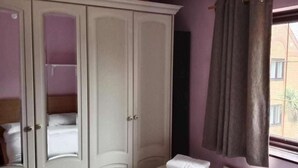 Een slaapkamer met een bed, een kledingkast, een radiator en een raam met gordijnen.