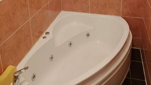 Une salle de bain avec une baignoire blanche, des murs recouverts de carreaux bruns et un tapis de bain jaune.