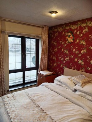 A hotel room with a bed, a nightstand, a window with curtains, and a floral wallpaper. - London - Waterfront House - Stay8 - Parking - Yard (London)