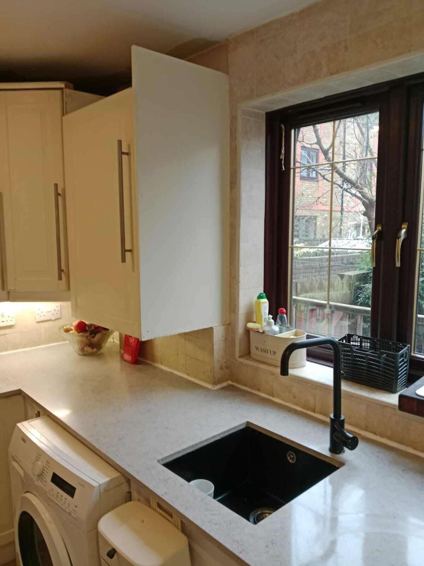A kitchen with a built-in washing machine, a sink, and a window with a view of the outside.