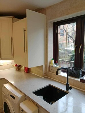Une cuisine équipée d’un lave-linge encastré, d’un évier et d’une fenêtre donnant sur l’extérieur.