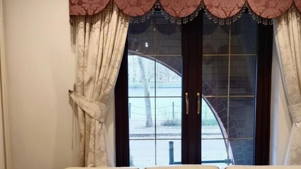 Un canapé beige dans une pièce dotée d’une grande fenêtre, de rideaux et offrant une vue sur un bâtiment à l’extérieur.