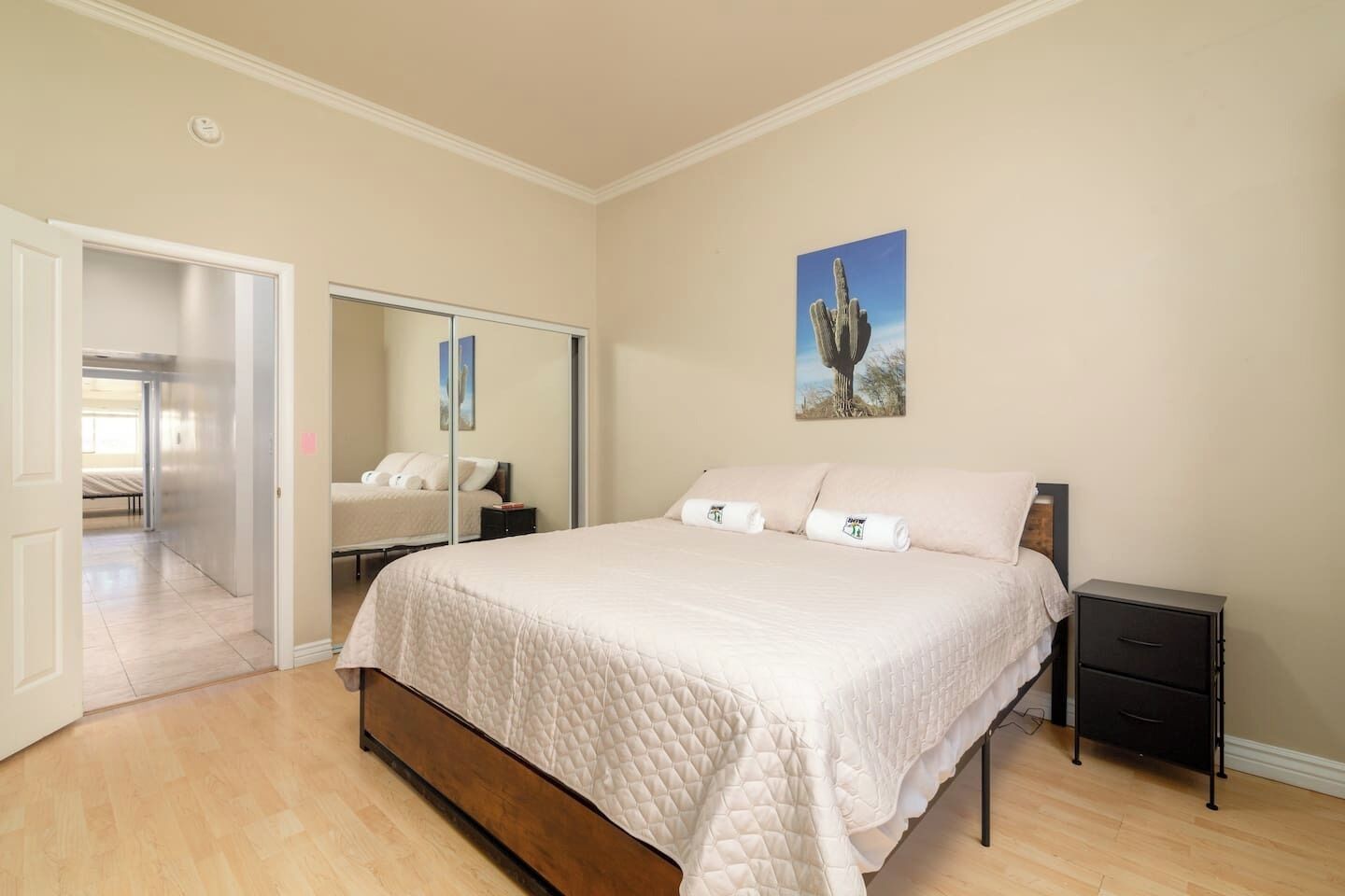 A bedroom with a large bed, a bedside table, a nightstand, a wardrobe, and a door leading to another room.
