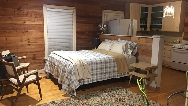 A cozy room with a bed, a small table, a chair, a kitchen area with a refrigerator and stove, and a patterned rug. - Desirable Elmwood location. Tudor style garage apt studio w/central heat& a/c. (Abilene)