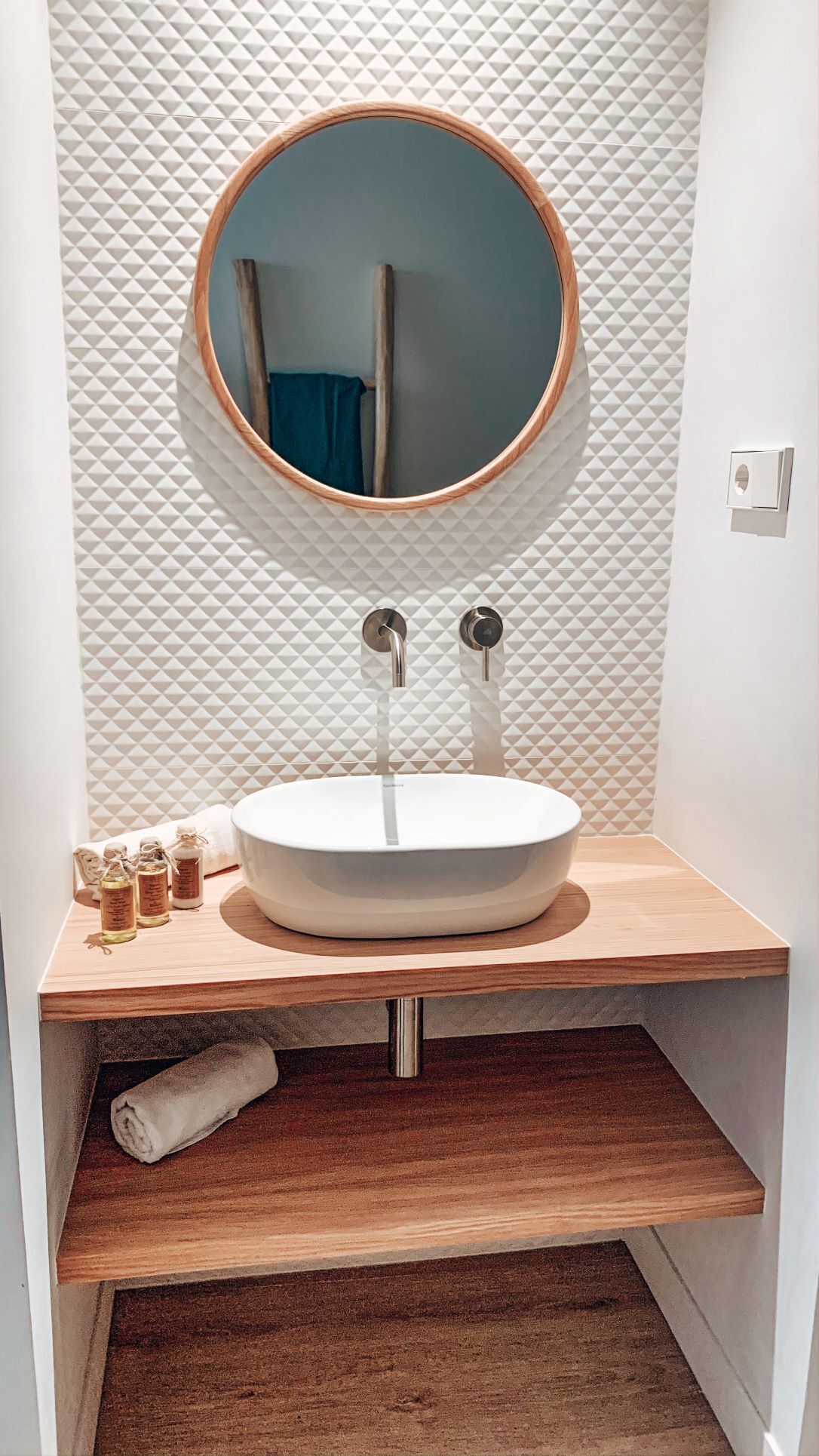 Un bagno con uno specchio rotondo, un lavandino bianco e un mobile vanitario in legno.