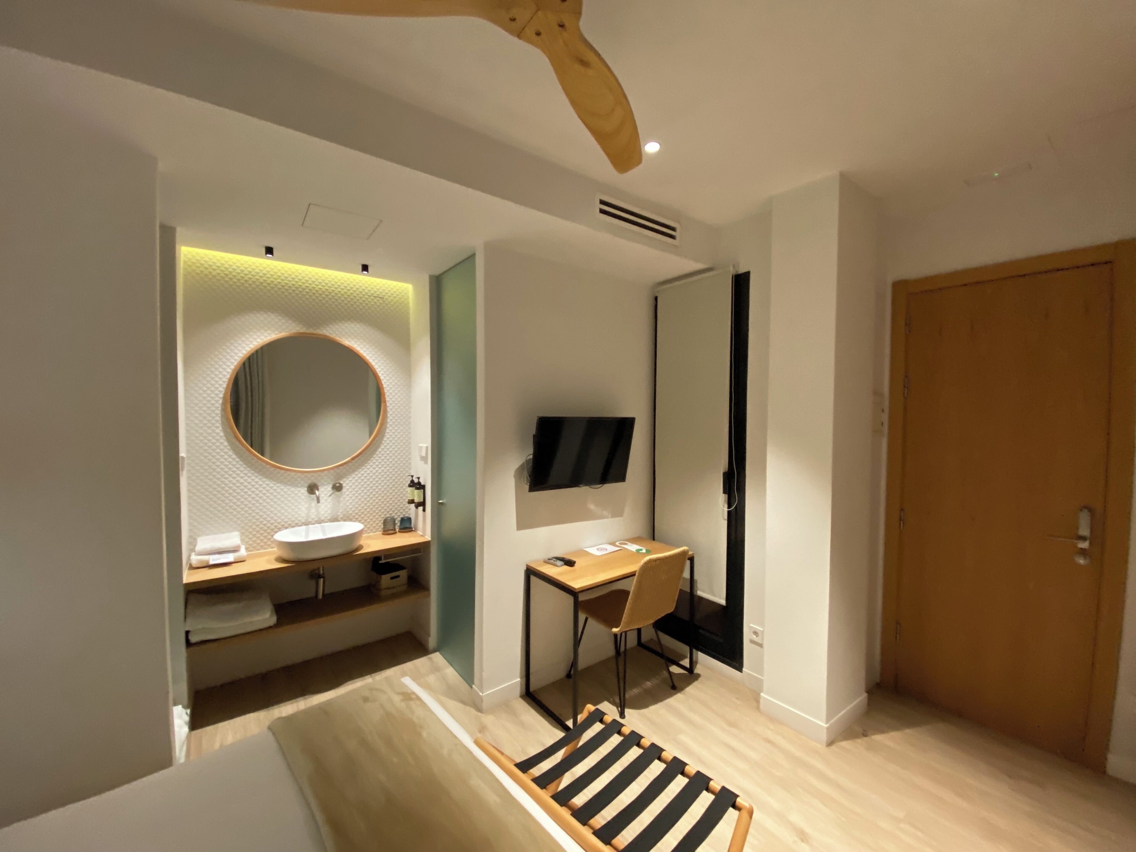 Un baño moderno con un espejo redondo, dos lavamanos, un escritorio de madera y un televisor.