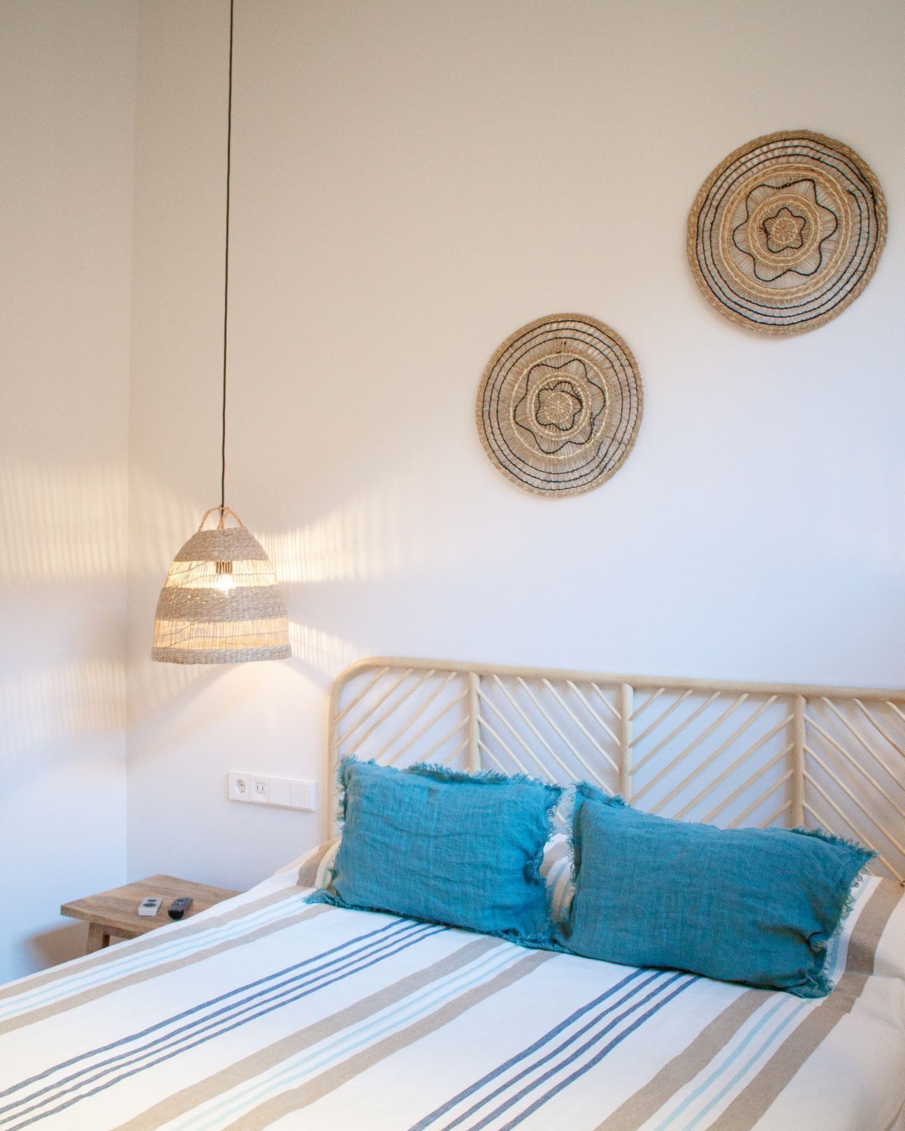 Una cama con una manta a rayas, un cojín azul y un tapiz tejido en la pared.