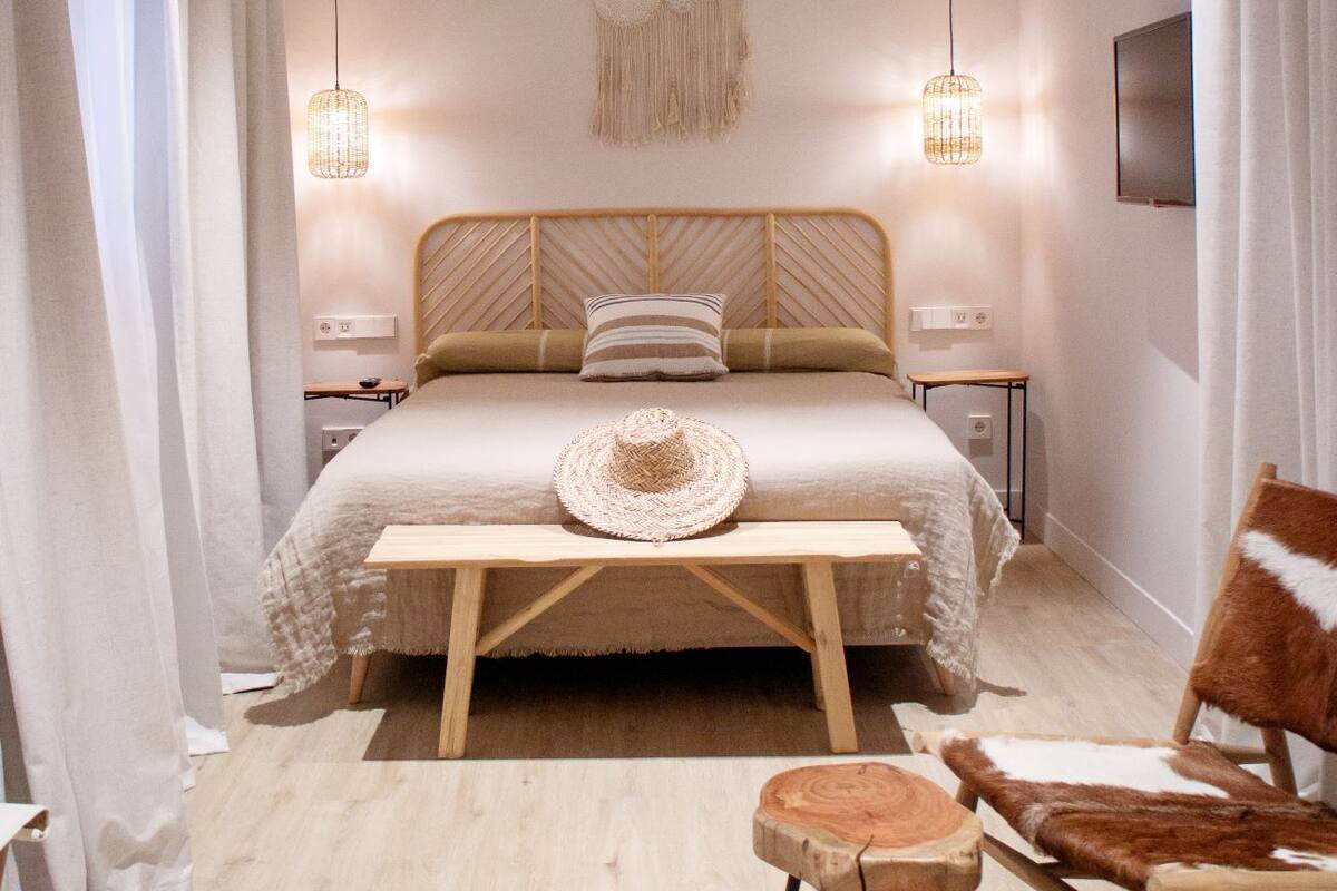 A bedroom with a bed, a wooden bench, a chair, a hanging light, and a ceiling fan.