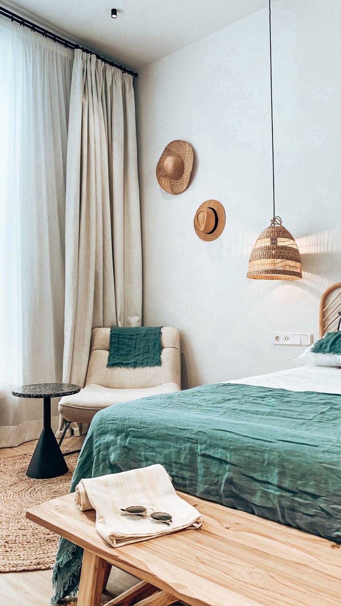 A bedroom with a bed, a chair, a small table, a hanging light, and a wall socket.