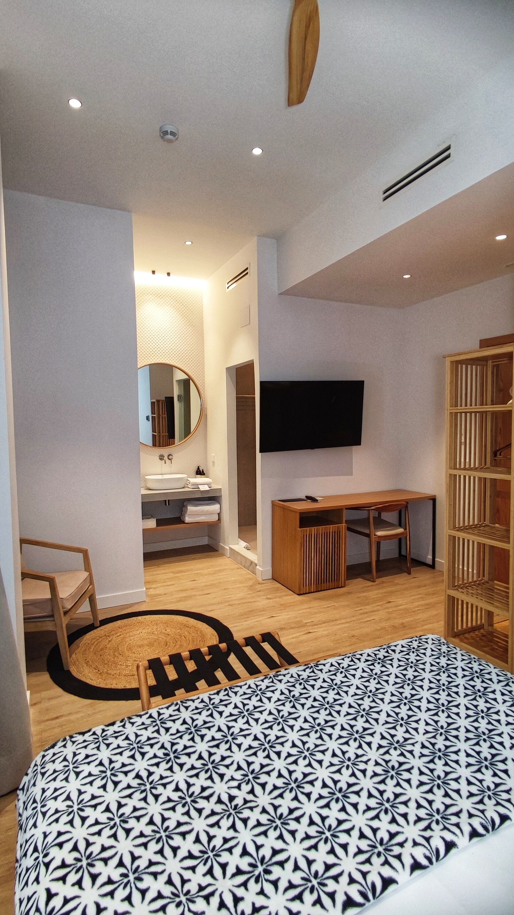 Ein modernes Schlafzimmer mit einem großen Bett, einem an der Wand montierten Fernseher, einem Holztisch und einem Spiegel.