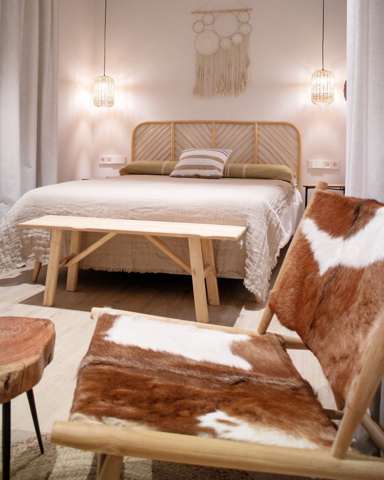 Un dormitorio con cama de madera, dos lámparas de noche, un tapiz en la pared y una silla marrón y blanca.