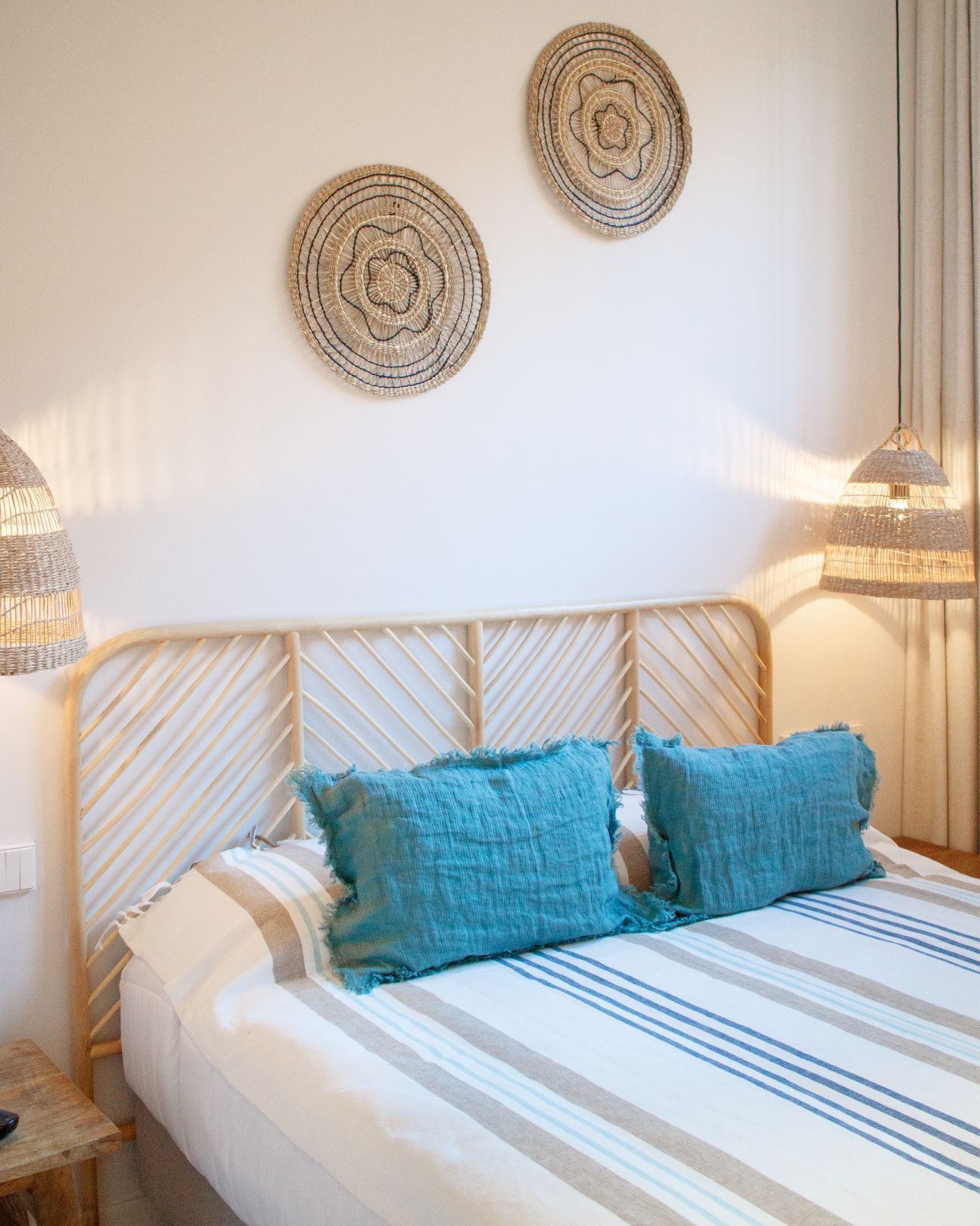 Una cama bien hecha con ropa de cama a rayas y dos almohadas azules, un cabecero de madera y dos adornos decorativos en la pared.
