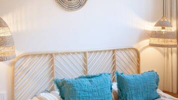 Una cama bien hecha con ropa de cama a rayas y dos almohadas azules, un cabecero de madera y dos adornos decorativos en la pared.