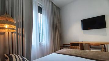 Una habitación de hotel con cama, escritorio, silla, televisor y ventana con cortinas.