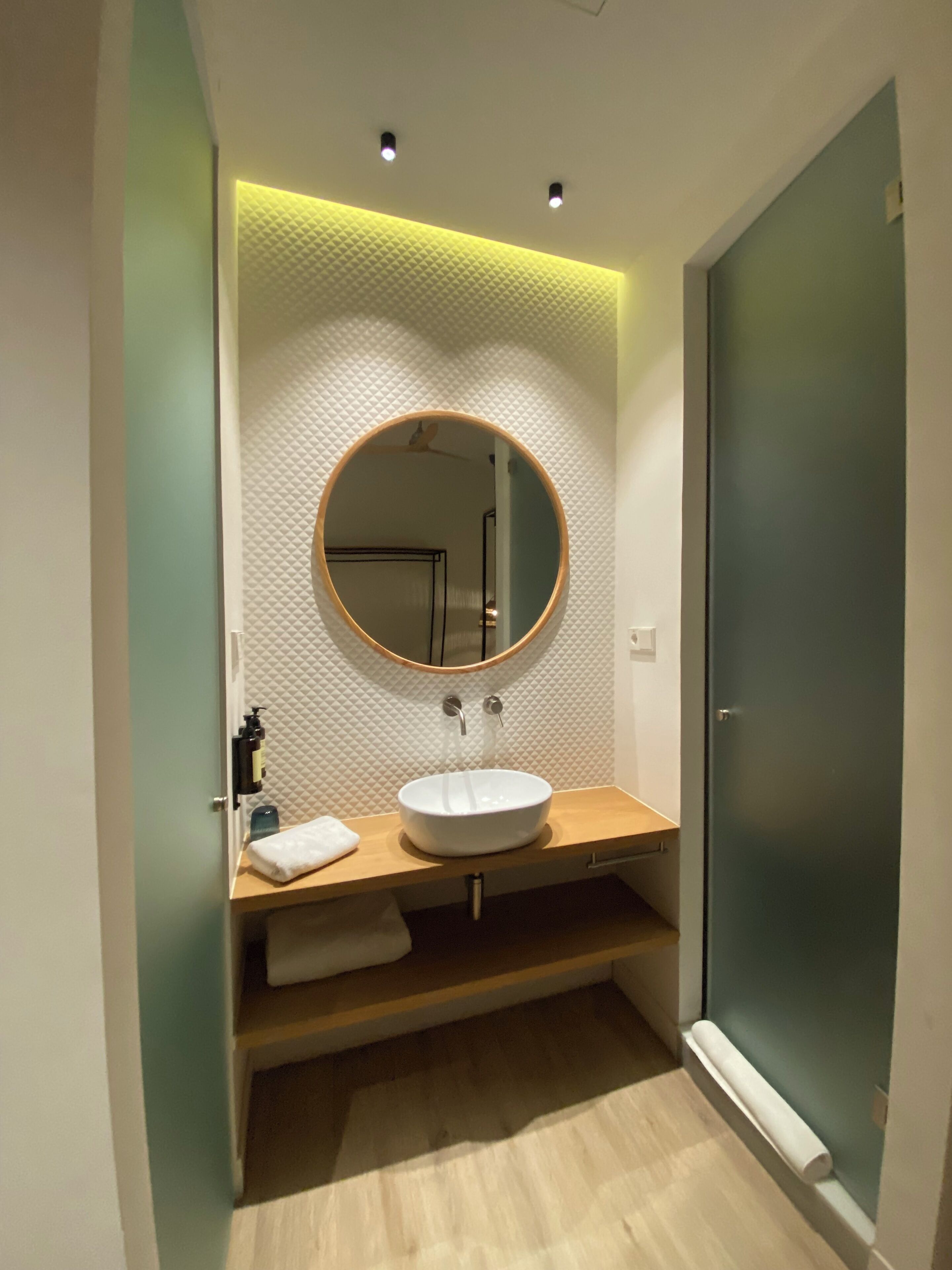 Un baño moderno con un espejo redondo, lavamanos blanco y tocador de madera.