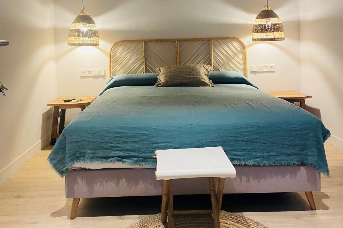 A bedroom with a bed, two nightstands, a ceiling fan, and two wall-mounted pendant lights.