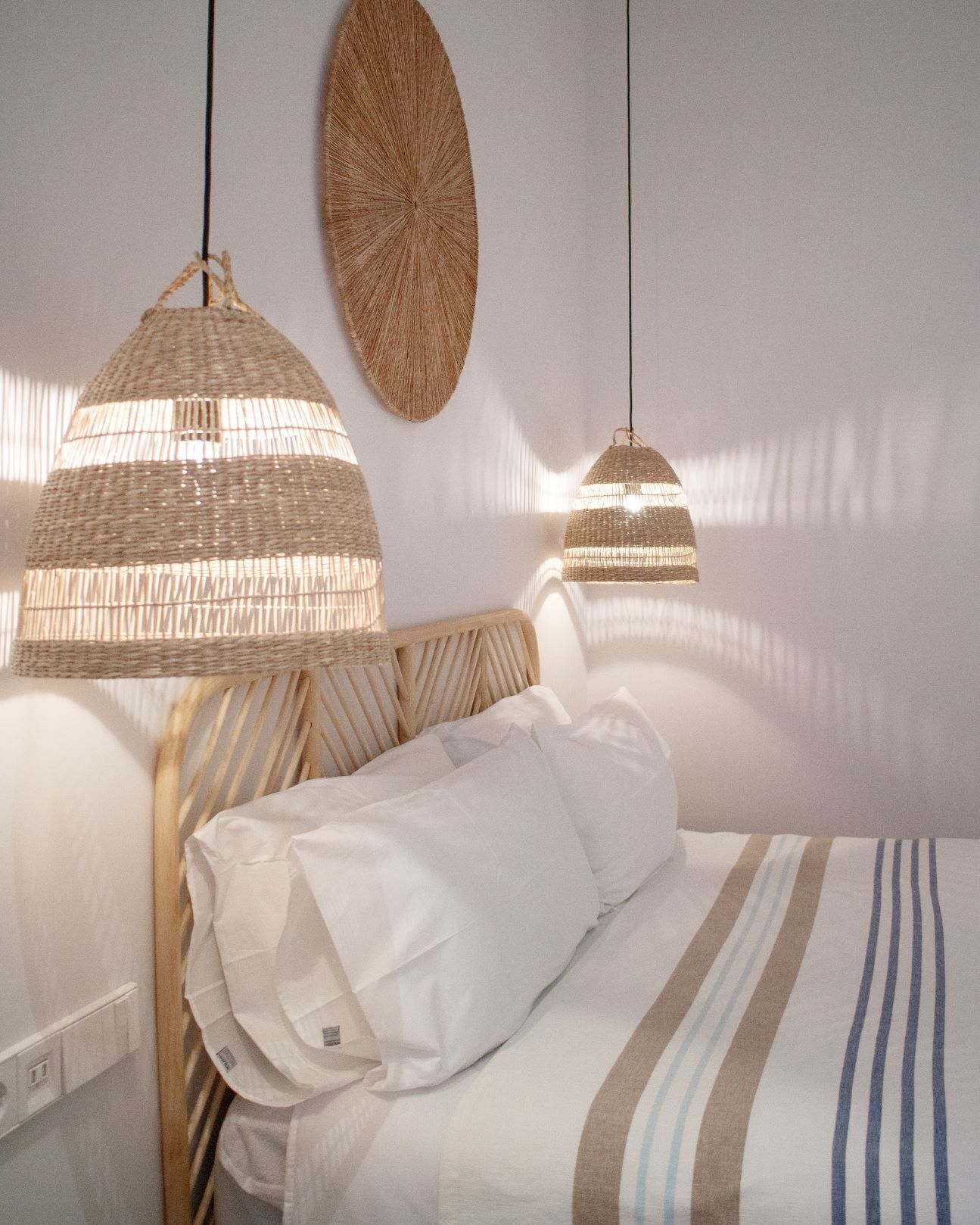 Una cama bien hecha con ropa de cama a rayas, dos lámparas colgantes tejidas y un tapiz de pared tejido.