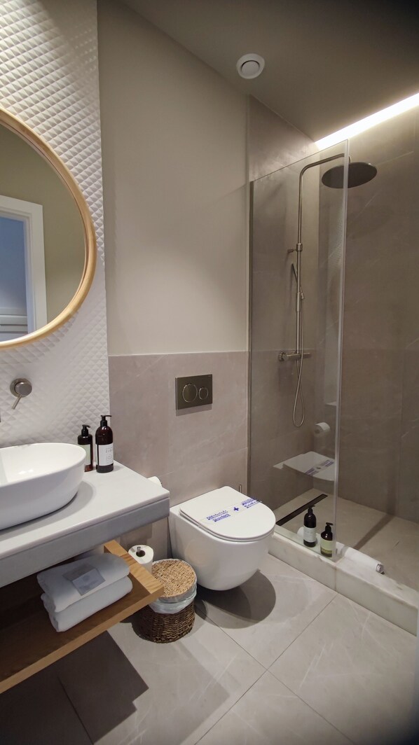 A modern bathroom with a round mirror, a toilet, a sink, and a glass-enclosed shower. - Casa du Soleil Hostal Boutique (Madrid)